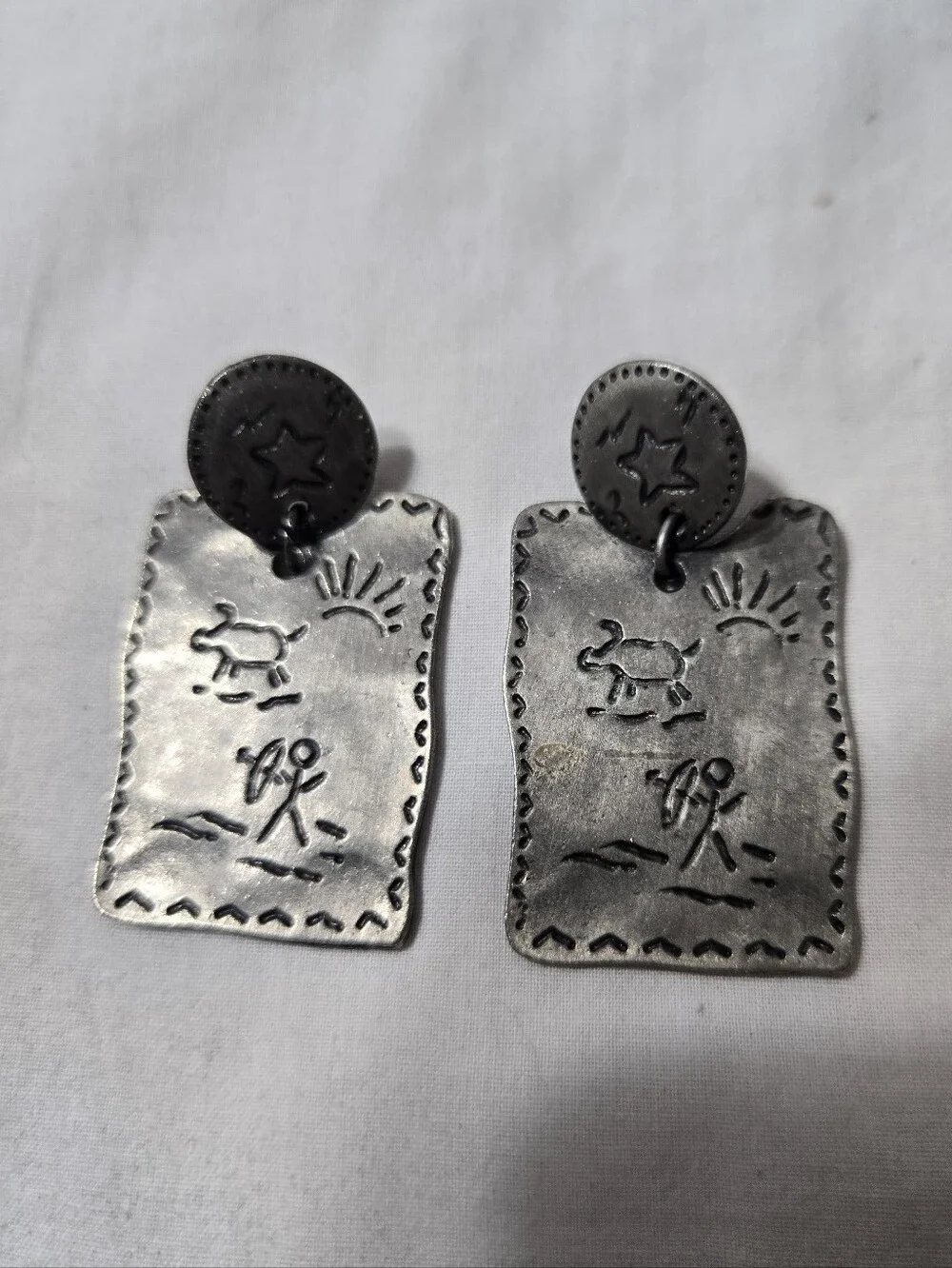 Vintage silver-tone drop earrings featuring embossed Southwestern petroglyph